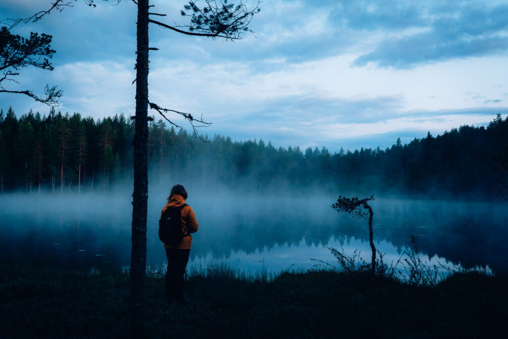 Hämärässä kuvassa veden päälle usvaa. Henkilö seisoo rannalla.